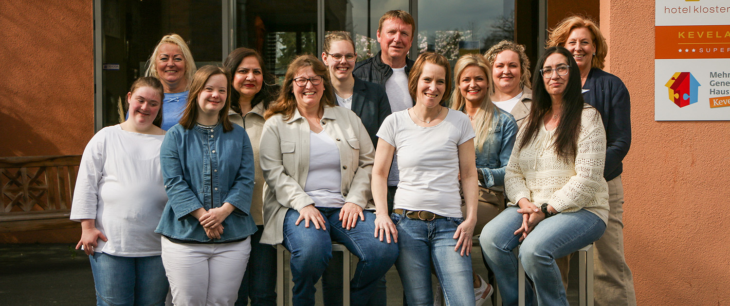 Das Team des Hotel Klostergarten steht für ein Gruppenfoto vor dem Haupteingang des Hotels. Insgesamt sind es zwölf Personen. Drei von ihnen sitzen auf einem Hocker.